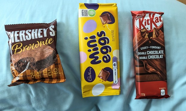 Image shows assorted international candy. A Hershey brownie, Cadbury mini egg candy bar, and a double chocolate KitKat.