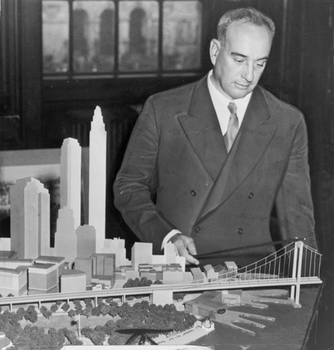 Robert Moses looking at a model of a bridge in a diorama of part of New York.
