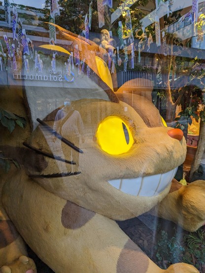 A large plush Catbus with lit up eyes, seen through a shop window