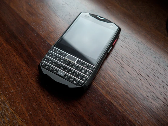 Photo of the Unihertz Titan Pocket laying on a wooden counter with its screen turned off. It's a mobile phone designed after the Blackberry phones of yesteryear, with a physical QWERTY keyboard underneath a square display.