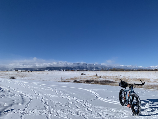 A blue fatbike on a snow covered Montana gravel road with winter pastures in the middle distance and the Beartooth Mountains in the background.