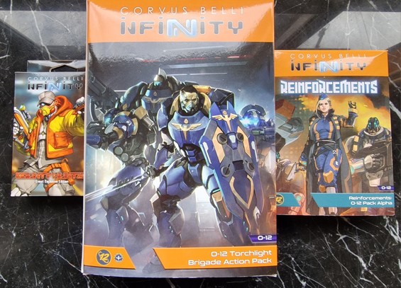 La imagen muestra tres cajas de Infinity por el lado de las ilustraciones, de izquierda a derecha: nuevo cazarrecompensas de la Adepticon 2024, Action pack de la brigada Torchlight y pack alfa de refuerzos de O-12