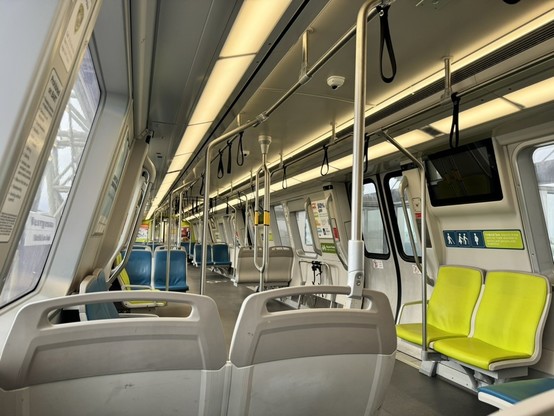 A modern BART light rail train car with green and blue seats, spaces for bicycles, and ample lighting from electric lights as well as windows.