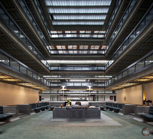 A well-kept reception area of a large modernist building. Four floors of balconies are visible above the desk, stretching off to connecting walkways. A granite desk with two lamps sits in the center. 