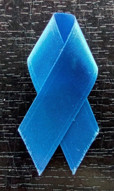 Photo: A blue ribbon with frayed edges on a scratched piece of black lacquered wood. Sunlight illuminates the grain in the wood.