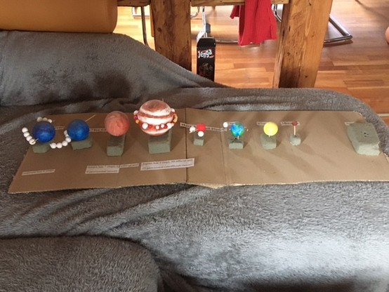 styrofoam balls colored to resemble the actual planets with their moons strung up on wire and circling the planets. The balls are attached to brown cardboard, and the planets are labeled