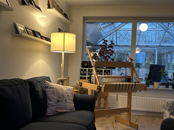 A handloom in the corner of a room illuminated by a floor lamp