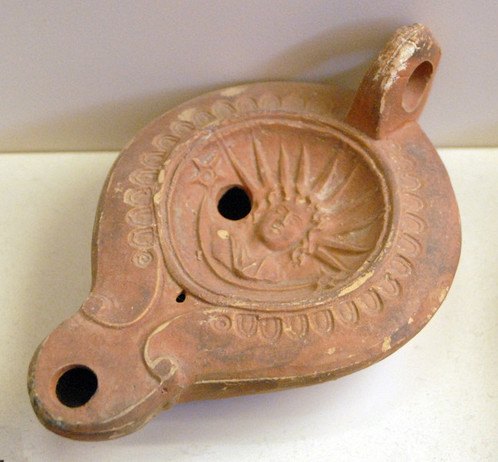 Roman terracotta oil lamp decorated with the image of Sol-Helios. He is depicted with a large ten-spike sunray crown. A stylised star appears next to him.