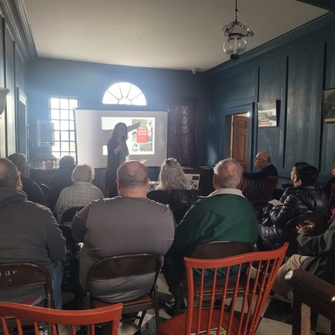 dimly lit photo of audience listening to me talk about Naming Gotham. I am blocking the projector.  sigh.  Beautiful 17th century hall with paneling and half-windows barely visible. 