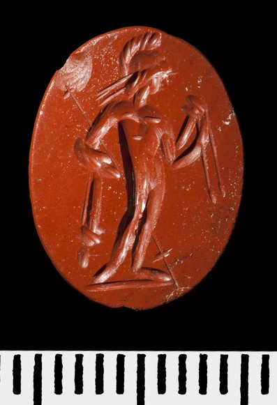 Red jasper, bevelled. Mars standing, wearing a crested helmet; the folds of a cloak over one arm, which cradles a long spear; in the left hand, a sheathed sword with dependent belt.