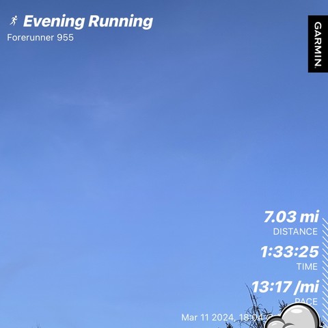 A screenshot of a fitness tracking app summarizing an evening running activity with clear blue sky in the background. The app displays distance 7.03 miles, time 1 hr 33 min 25 sec, pace 13 min 17 sec/mile, and the date March 11 