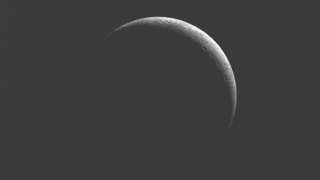 Black background. The moon fills most of the image. A thin crescent part of the moon (upper right) is dim but details (craters) are discernible. The rest of the moon is dark with no details discernable.