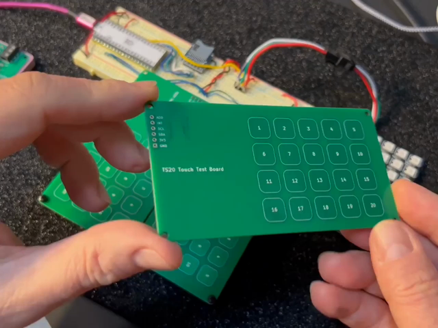 Two hands hold a blank PCB with 20 touch pads on one side and traces on the other. Underneath, two of the same kind of PCBs are plugged into a breadboard with a Raspberry Pi Pico and a grid of LEDs, and tapping on the pads lights up a corresponding LED.