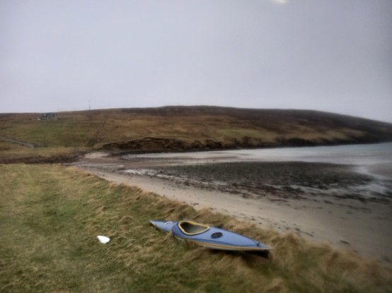 Wiese, Strand und der Meeresboden bei Ebbe. Im Hintergrund ein Hügel, vorne im Bild liegt ein Kajak.