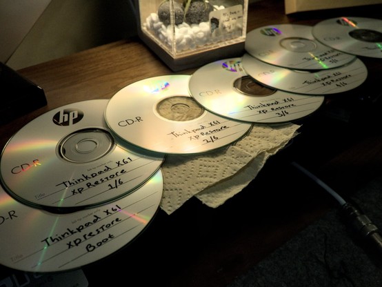 Photo of the seven CDs I had to burn stacked out like a spread out deck of cards. Each CD has "Thinkpad X61 XP Restore X of 6" written on it in felt, with the X being the numbers one through six. The first disc is sub-titled "boot" as it is not technically part of the XP restore set, but the rescue and restore boot environment Lenovo used at the time for these devices.