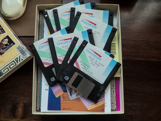 Photo showing the 8 2.5 inch floppy disks laying on top of a stack of other contents the game comes with.