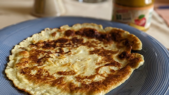 Ein großer Teller mit einem #Eierpfannenkuchen. Im Hintergrund ein Glas mit Apfelmus. 