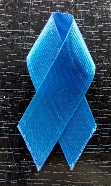 Photo: A blue ribbon with frayed edges on a scratched piece of black lacquered wood. Sunlight illuminates the grain in the wood.