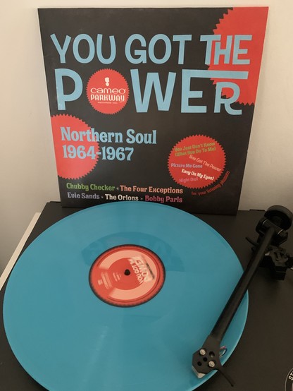 Eine blaue Schallplatte auf einem Plattenteller mit einer Plattenhülle im Hintergrund von der Northern-Soul-Compilation "You Got The Power" von Cameo Parkway Records mit Künstlern aus den Jahren 1964-1967.