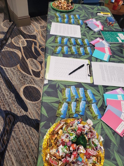 Picture of a busy hotel carpet and a table with a cannabis leaf tablecloth, with business cards, clipboards, and blank journals arranged on display.