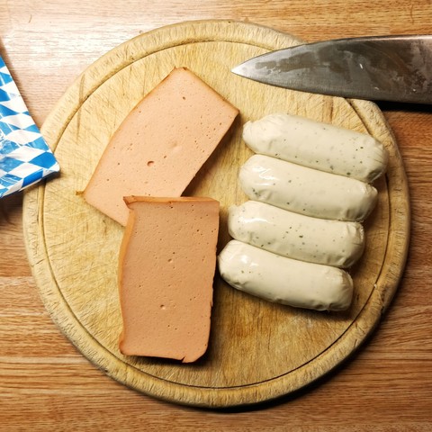 Veganer Leberkäse und vegane Weißwürste von Greenforce warten auf die Zubereitung auf einem Brett.