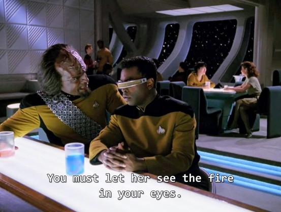 TNG scene. We're in Ten Forward and we're looking out from behind bar with tables and lots of off duty Starfleet folks just chilling and relaxing at tables in the background. There's a nice big window out to space. Front and center at the bar is Worf and Geordi. Worf is a Klingon with a large forehead of pointed ridgeloaf who is swol and tough (but also sensitive ). Geordi is human but wears a visor over his eyes because he cannot see through his eyes normally so he views the world through interpreted vision created by this head visor instead of his eyes. 
In picture 1, Worf is turned and speaking animatedly towards Geordi. Closed caption reads, "You must let her see the fire in your eyes." 
Picture 2 is Geordi, with visor, looking dumbfounded back at Worf with a wtf face. 