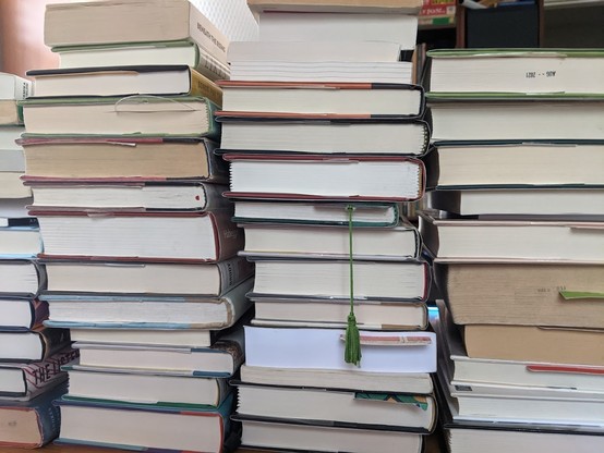 Upper view of three stacks of hardcover books that fill the image top-to-bottom with a few bookmarks protruding. 