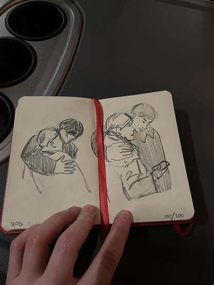 Sketchbook with two pencils drawings of the same couple: a man is bending down to kiss a woman, a ben is hugging a woman and looking at her phone in her hands 