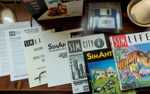 Photo of all the contents of the game box, from some installation related flyers to a quick start  guide to three full manuals, one for each game. Sim Life is the thickest of all three. The SimCity manual as-well as all flyers are in black and white, but the manuals for SimAnt and SimLife are in color.