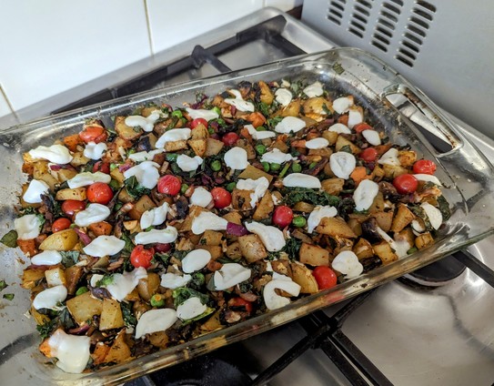 Rectangular glass dish on hob.
Potato bake has tomatoes, kale and mozzarella on top.