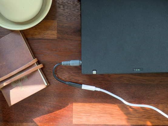 A top-down photo showing a USBC to DC charging dongle connected to my Thinkpad X61, with the laptop's power and battery indicator lights both on indicating that it's being powered by the power supply. It's a short dongle, maybe 10 centimeters long, and has the specific barrel plug type this laptop uses on one end, and a USBC female port on the other end.