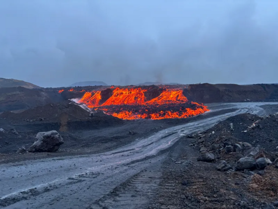 Foto in der Dämmerung, Lava strömt über eine Kante mehrere Meter tief in den Tagebau. 