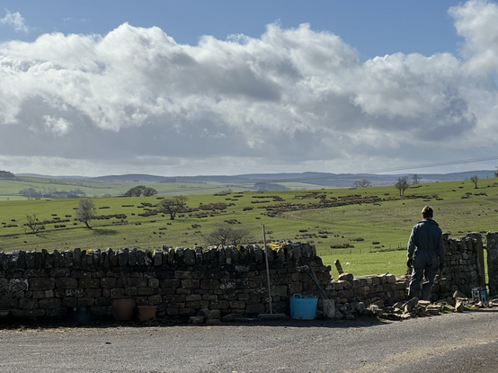 Jonny the dry stone wallet repairs a section of wall with a view of the valley in the background
