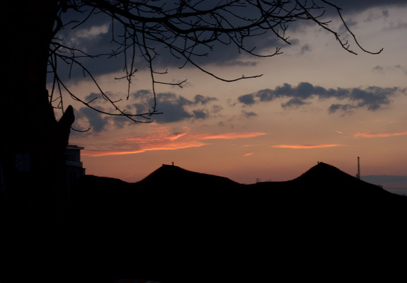 Motiv: Das Motiv des Bildes ist eine Silhouette eines Baumes und Hausdächern mit einem Sonnenuntergang im Hintergrund.

Bildformat: Das Bildformat ist ein Querformat.

Genre: Das Genre des Bildes ist Landschaftsfotografie.

Hintergrund: Der Hintergrund des Bildes ist ein Himmel in verschiedenen Rot- und Orangetönen.

Farben: Die Farben des Bildes sind warm und lebendig. Der Himmel ist in verschiedenen Rot- und Orangetönen gehalten, während der Hügel in einem dunklen Braun gehalten ist.
