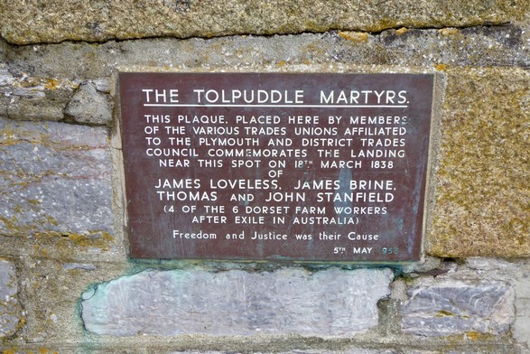 A plaque set in a wall reads, “THE TOLPUDDLE MARTYRS.
THIS PLAQUE. PLACED HERE BY MEMBERS OF THE VARIOUS TRADES UNIONS AFFILIATED TO THE PLYMOUTH AND DISTRICT TRADES COUNCIL COMMEMORATES THE LANDING NEAR THIS SPOT ON 18TH MARCH 1838
JAMES LOVELESS, JAMES BRINE, THOMAS AND JOHN STANFIELD
(4 OF THE 6 DORSET FARM WORKERS
AFTER EXILE IN AUSTRALIA)
Freedom and Justice was their Cause
5TH MAY1956”