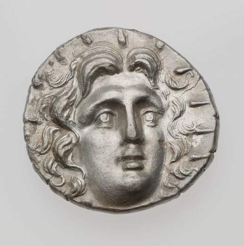 Tetradrachm of Rhodes, a silver coin with the head of Helios, struck under Aetion. The god is depiced with lush, wavy hair and an aureola. 3rd–2nd century BCE.