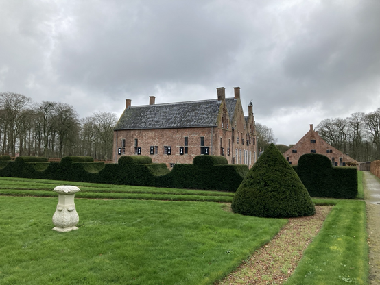 Dit deel vd tuin bestaat vooral uit gras, een in golven geschoren taxushaag enrode steenslag op het geometrische padenstelsel. Achtergrond de achterkant vd borg en de zijkant van het schathuis onder grijze hemel 