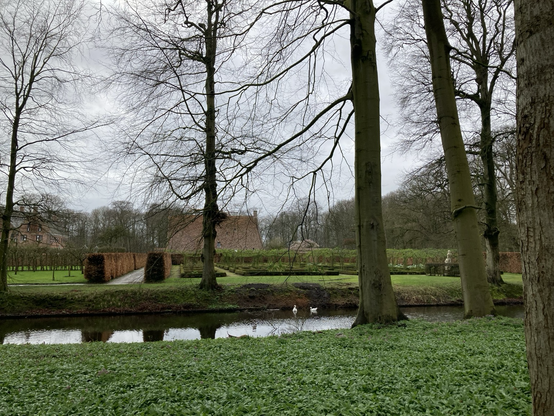 Blik over de gracht met eendjes naar groentetuin en schathuis 
