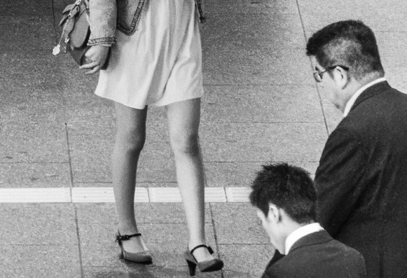 Black and white photograph of woman's legs with men looking in that direction on a street in Osaka, Japan.