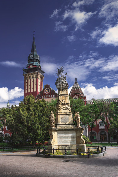 Walking through Subotica, a beautiful city located in the north of Serbia, which is full of old architectural objects, churches, cathedrals, monuments, and various other sacral buildings and cultural sights, I came across this magnificent monument. You can see the gorgeous City Hall building Behind which is also one of the main sights of Subotica.
Holy Trinity monument in Subotica, Serbia is located on the Republic Square near the impressive City Hall and the Blue fountain. It is the work of Karl Salzer and was set up in 1815 on the former market place. The government made the decision to move the monument to the square between the Cathedral of St.Theresa of Avila and the building of the Subotica Diocese In 1964. where it was until December 2014. It was restored at the initiative of the Hungarian National Council at the expense of the landowner Matija Vojnić from Bajsa In 2016. and was returned to its nowadays location. The restoration work was performed by the academic sculptor Karolina Biaci. This monument is surrounded by trees and greenery and there are benches as well if you want to seat and rest in the park enjoying in view. It is one of the main cultural sights in Subotica and you should see it if you ever visit this beautiful town in the north of Serbia.
Somewhere in May. Subotica, Vojvodina, Serbia. From the Monuments and Sculptures collection.