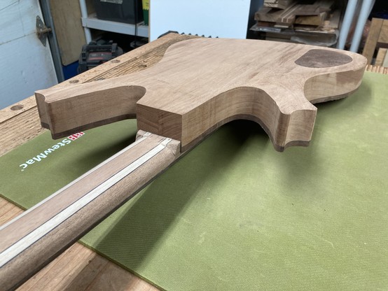 A baritone guitar in progress sits on a workbench, atop a green rubber mat.