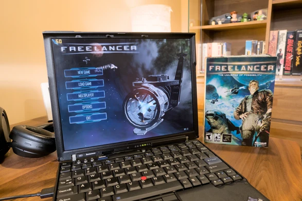 Photo showing the Freelancer main menu displayed on my Thinkpad X61, with the small physical game box standing next to the laptop. It's a carton box release but as with many games released in the early 2000s and onwards, the box sizes got smaller. This size is about the size of a typical DVD case, though it's twice as thick.