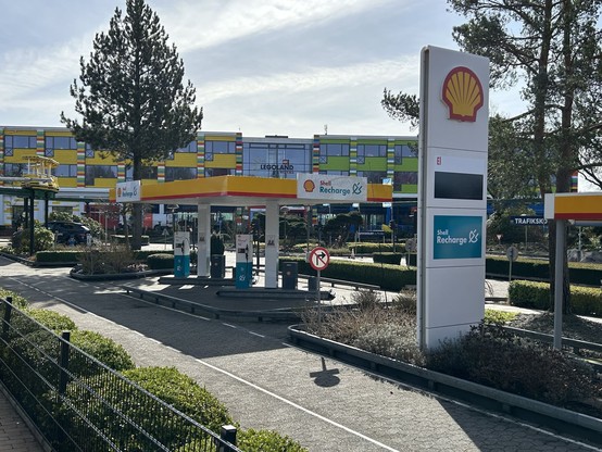 Shell-branded forecourt with El (electricity) price display and 'Shell Recharge' branding. Multiple EV chargers under the forecourt roof. In the background: LEGOLAND building.