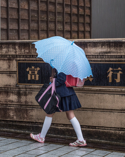 Schoolgirl with blue umbrella walking in the rain in Japan.