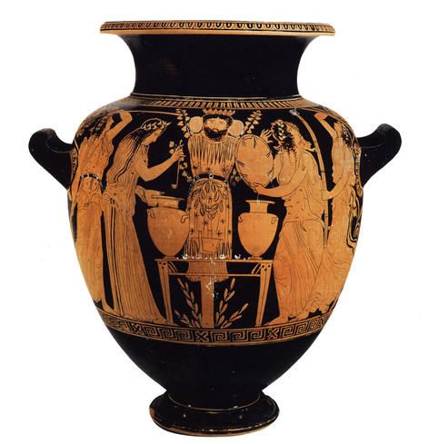 Red-figure vase painting of women or maenads with thrysoi and tambourines dance around a pillar idol of #Dionysos, festooned with branches and set before a table holding two large stamnoi (storage vessels) from which one of the ladies ladles wine into a skyphos cup.