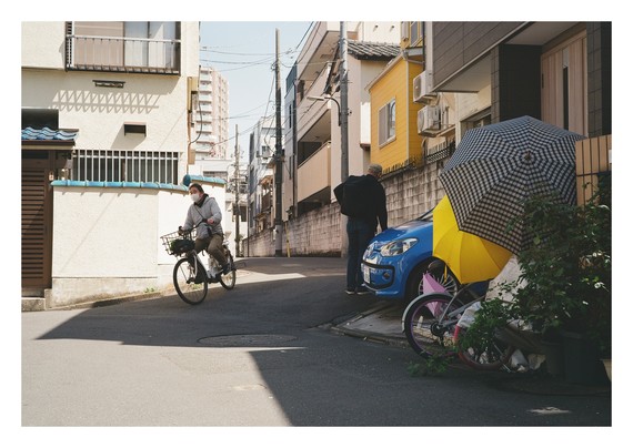 A yellow umbrella, a blue car, and a bicycle riding past them.