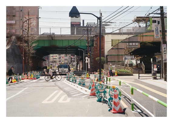 A train underpass with a bicycle riding past it, and a few traffic cones in the foreground