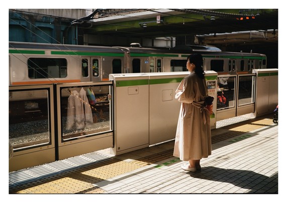 A woman in the traditional beige trenchcoat of Japan, standing in beautiful light on a train track.