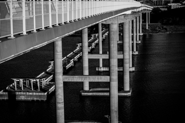 A black and white photo taken from the walkway of the Arthur Ravenel bridge in Charleston SC, showing the underside of the bridge and nearby walking pier.