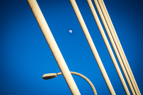 A color photo of 5 cable supports on the Arthur Ravenel bridge in Charleston SC taken close up.  The moon in gibbous shape is between 2 of the cables.